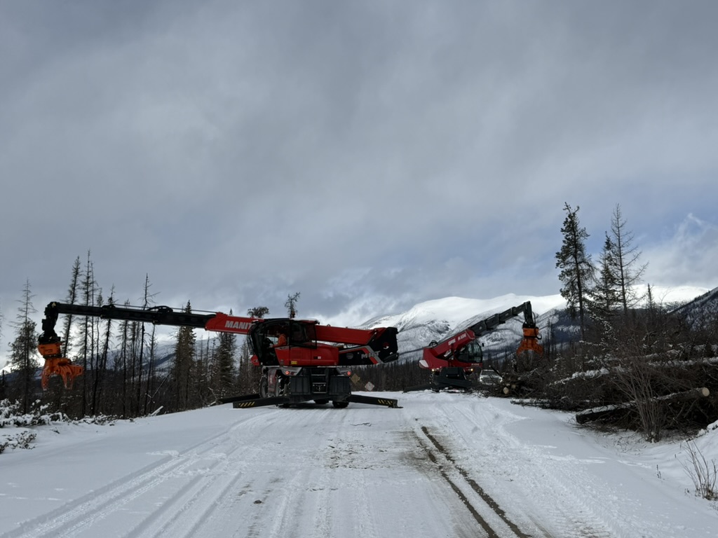 Two Manitou boom units removing danger trees along a snowy mountain road
